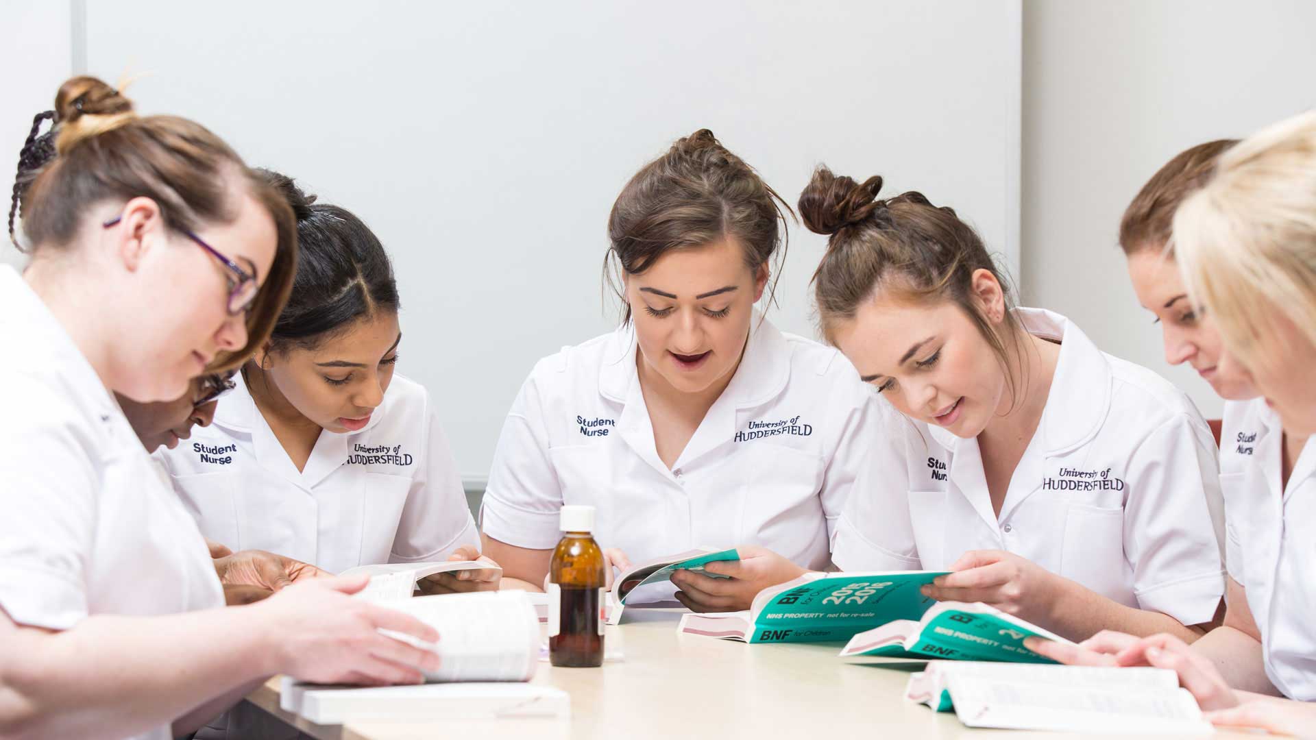 A group of students sit around a table, looking through a medical book